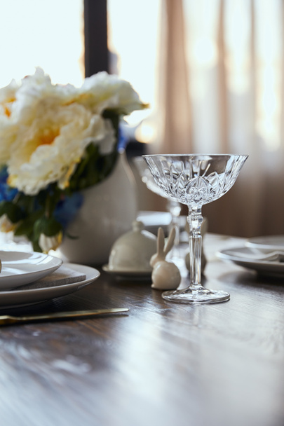 selective focus of crystal glass, bouquet in vase and decorative bunnie on wooden table at home - Foto, Imagem