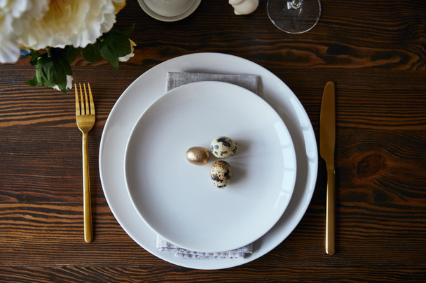 pohled shora Křepelčí vejce na bílých talířích poblíž vidličku a nůž na dřevěný stůl - Fotografie, Obrázek