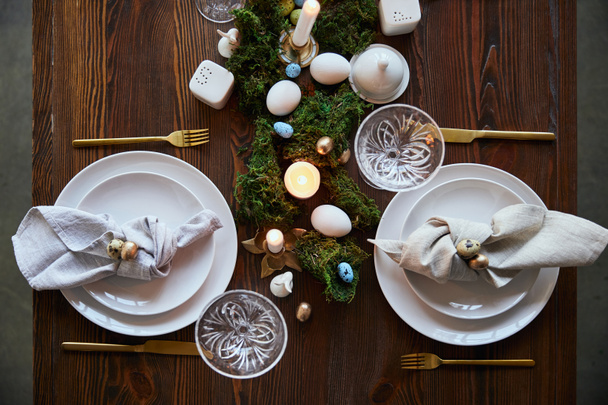 vista superior de huevos de codorniz en servilleta y platos cerca de musgo verde, velas y vasos de cristal en mesa de madera
 - Foto, Imagen