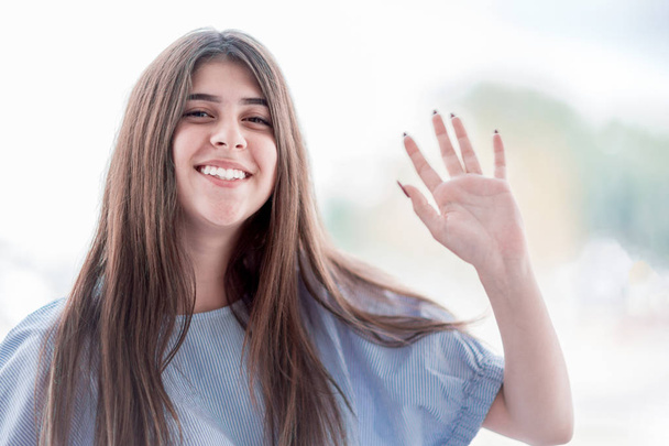 Smiling girl with thick eyebrows waving her hand - Foto, afbeelding