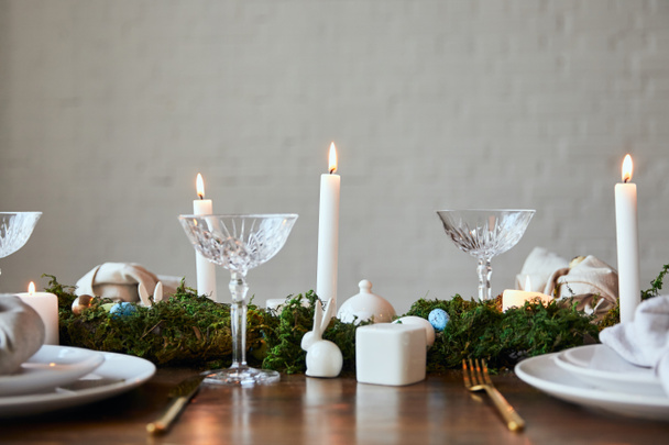 crystal glasses, burning candles, green moss and  quail eggs on napkin and dishware table at home - Фото, изображение