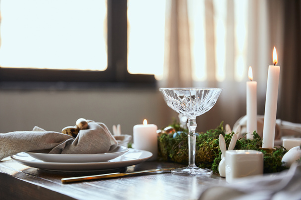 szelektív összpontosít fürjtojás, szalvéta és zöld moha, égő gyertyák és üveg kristály fából készült asztal otthon közelében lemezek - Fotó, kép