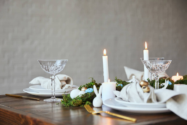 selective focus of quail eggs on napkin and plates, green moss, candles, crystal glasses and decorative bunnie on wooden table at home - Photo, Image