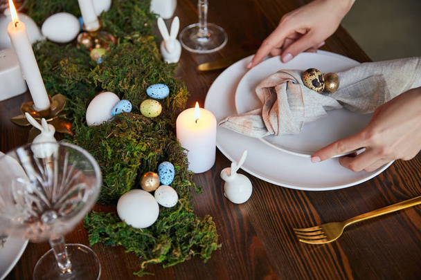 vista ritagliata di donna che mette piatti vicino a candele ardenti e muschio sul tavolo di legno a casa
 - Foto, immagini