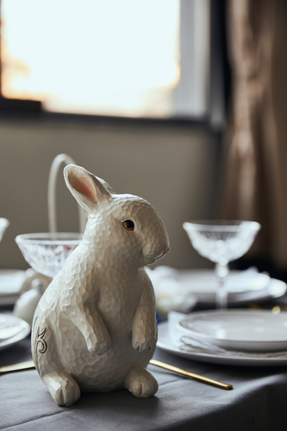 selective focus of decorative bunnie near plates and crystal glasses on table at home - Fotoğraf, Görsel