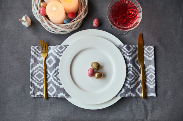 top view of plates with cloth napkin, eggs and burning candles in basket, wine in crystal glass on table at home - Foto, Bild