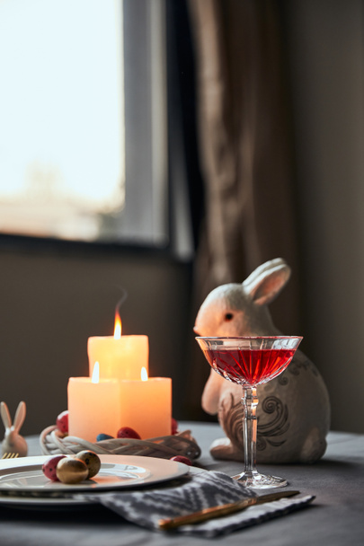 селективная фокусировка тарелок с яйцами, вином в хрустале и декоративным кроликом на столе дома
 - Фото, изображение