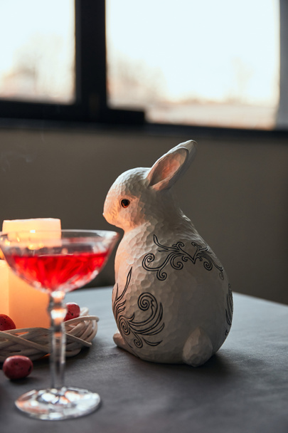 decorative bunnie, eggs, wine in crystal glass and burning candles on table at home - Photo, Image