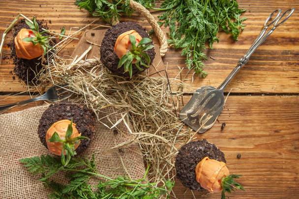 Bolo de Páscoa em fundo de madeira com terra de biscoito e cenouras de morango
 - Foto, Imagem