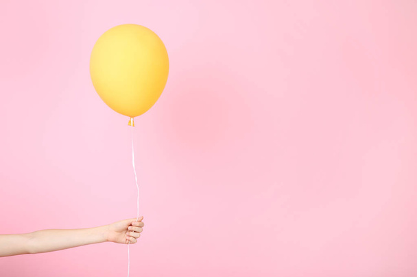 Female hand holding yellow balloon on pink background - Foto, afbeelding