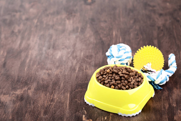 Dry pet food in bowl with toys on brown wooden table - Fotografie, Obrázek