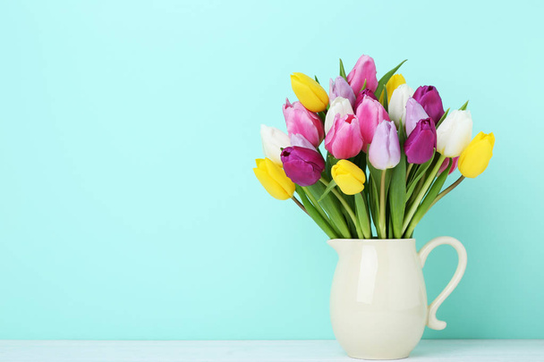 Bouquet of tulips in jug on wooden table - Zdjęcie, obraz