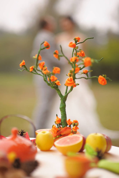 Matrimonio autunnale. Ritratto esterno di baciare gli sposi con un albero genealogico di origami arancione brillante nel parco autunnale e foglie gialle. Tavola di frutta nuziale.  - Foto, immagini