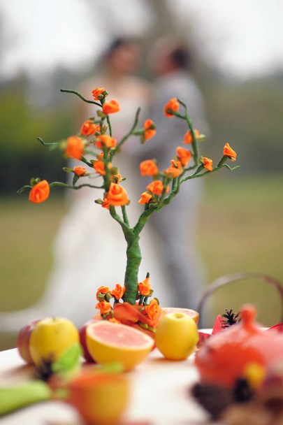 Autumn marriage. Outdoor portrait of kissing newlyweds with bright orange origami family tree in autumn park and yellow leaves. Wedding fruit table.  - Photo, Image