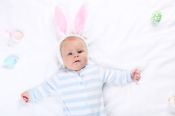 Baby boy in rabbit ears lying on white bed - Fotó, kép