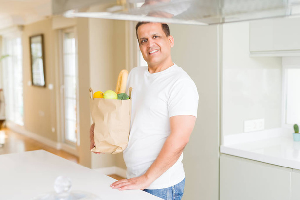 Mann mittleren Alters hält Einkaufstasche voller Gemüse zu Hause - Foto, Bild