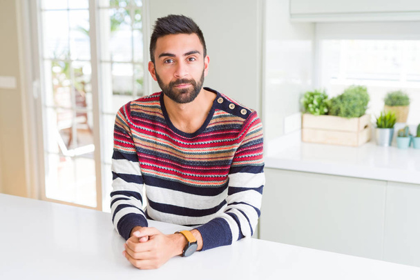 Handsome hispanic man wearing stripes sweater at home with serious expression on face. Simple and natural looking at the camera. - Photo, Image