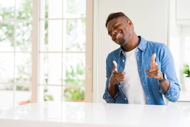 Bonito homem afro-americano em casa apontando os dedos para a câmera com rosto feliz e engraçado. Boa energia e vibrações
. - Foto, Imagem