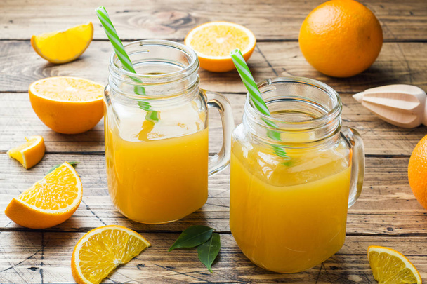 Orange juice in glass jars and fresh oranges on a wooden rustic background. - Photo, Image