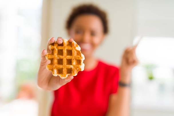 Joven mujer afroamericana comiendo gofre dulce muy feliz señalando con la mano y el dedo hacia un lado
 - Foto, Imagen