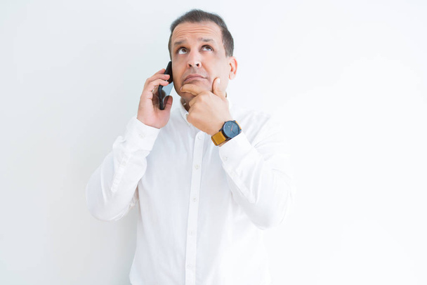 Middle age man calling using smartphone serious face thinking about question, very confused idea - Фото, изображение