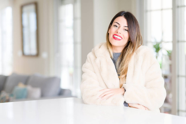 Young beautiful woman wearing winter fur coat at home happy face smiling with crossed arms looking at the camera. Positive person. - Photo, Image