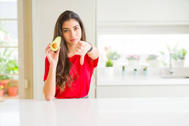 Fiatal nő eszik egészséges avokádó Haragos arc, negatív előjellel mutatja nem tetszik a hüvelykujját lefelé, elutasítás koncepció - Fotó, kép