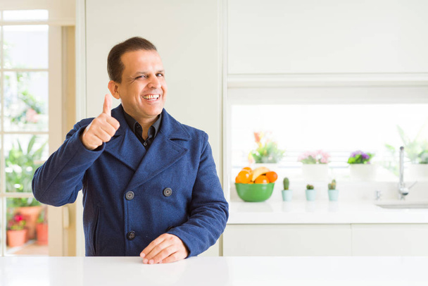 Middle age man sitting at home doing happy thumbs up gesture with hand. Approving expression looking at the camera with showing success. - Fotografie, Obrázek