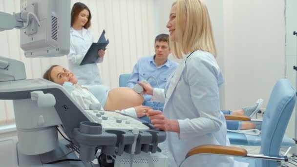 Lekarz wykonuje badanie ultrasonograficzne dla kobiety w ciąży w szpitalu. Szczęśliwy człowiek trzymając żonę ręką i oglądając ekran - Materiał filmowy, wideo