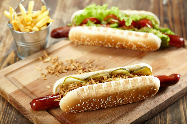 Dva hot-dogy s hranolky na dřevěném prkénku. Nezdravé potraviny - Fotografie, Obrázek