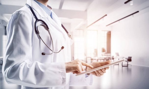 Close up of successful female doctor touching tablet with finger while standing indoors of white hospital building . Medical industry concept by means of confident doctor - Foto, Bild