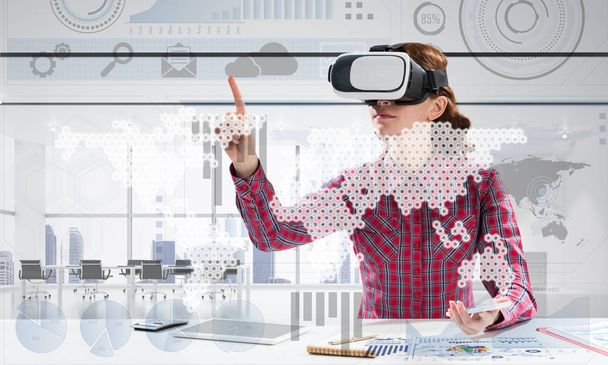 Horizontal shot of young and beautiful woman in checkered shirt using VR headset and media interface while sitting inside bright office building. Educational process with help of new technologies - Фото, зображення