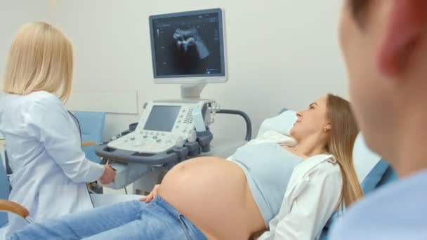 女性の医師は、妊娠中の女性に超音波スキャンの写真を与えます。少女は新生児を期待していました。母性の概念. - 映像、動画