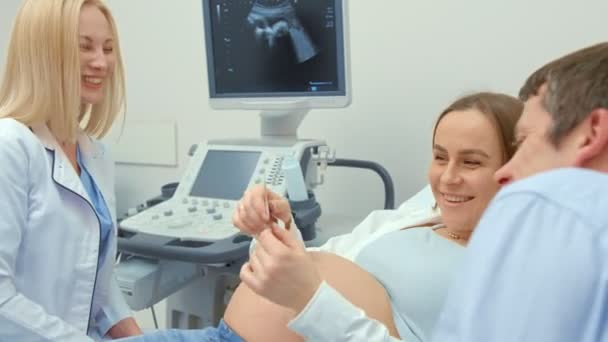 女性の医師は、妊娠中の女性に超音波スキャンの写真を与えます。少女は新生児を期待していました。母性の概念. - 映像、動画