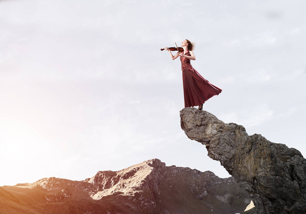 Young attractive girl playing violin standing at top of rock - Фото, изображение