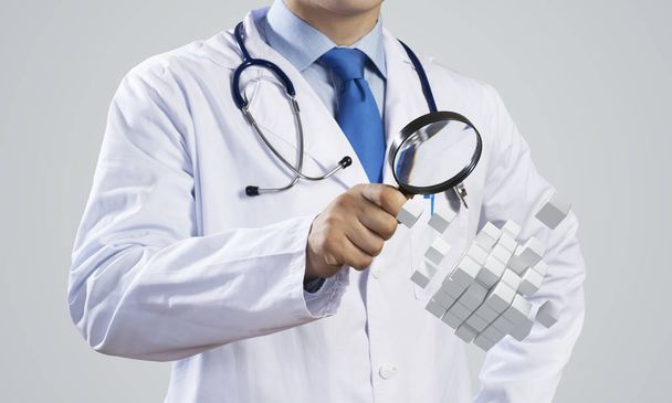 Horizontal shot of young doctor in white medical uniform studying multiple cubes in his hands while standing against gray dark wall on background. - Photo, Image