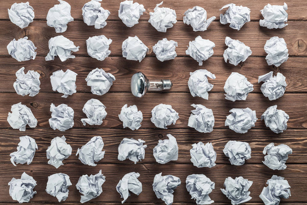Incandescent bulb and crumpled white paper balls on brown wooden table - Photo, Image