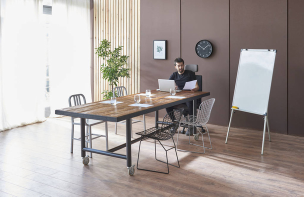Ruskea seinä ja puinen tausta, puinen pöytä, toimistohuone tuoli kasvi ja kartonki. Mies tekee töitä.. - Valokuva, kuva