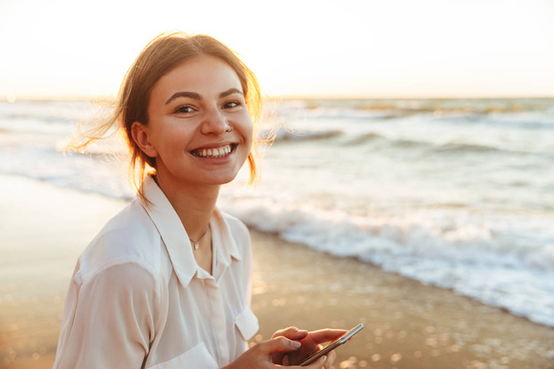 Image of happy woman 20s smiling and using cell phone, while wal - Foto, Imagen