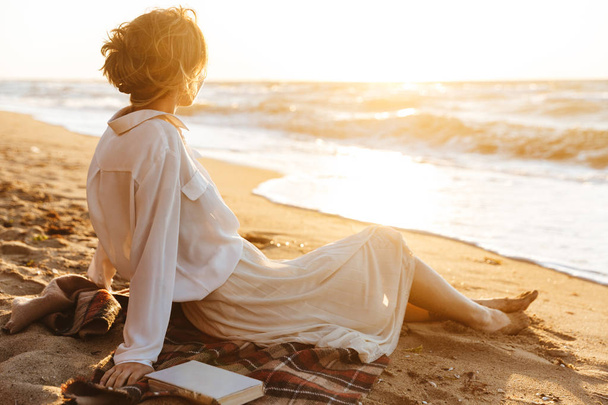 Image of beautiful woman 20s sitting on sand and looking at sea, - Valokuva, kuva