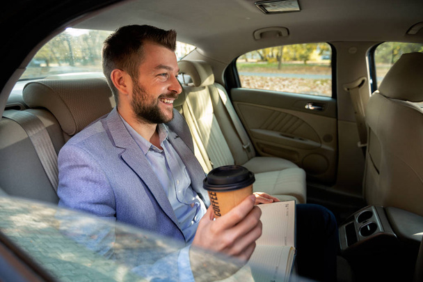 Man drinking coffee on the back seat of the car - Фото, зображення
