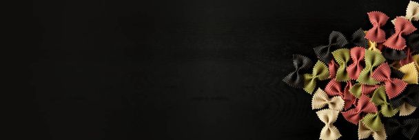 farfalle Farfallini cru colorido macarrão italiano em um fundo de madeira preto texturizado. Vista de perto a partir do topo. Espaço livre para texto. Banner
 - Foto, Imagem
