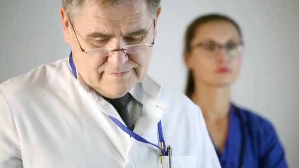 Il medico ascolta attentamente il paziente e prende appunti. Infermiera in piedi sullo sfondo della clinica. Primo piano
. - Filmati, video