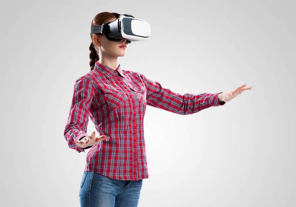 Young woman in checked shirt wearing virtual helmet against gray background - Foto, Bild