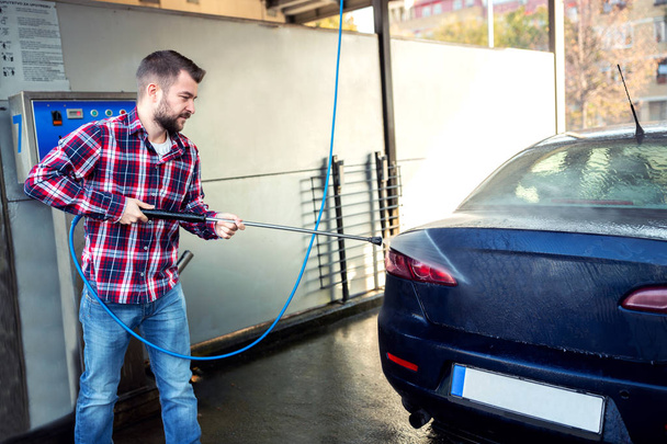 Handsome guy in blue jeans washing the back of his car - Foto, Imagem