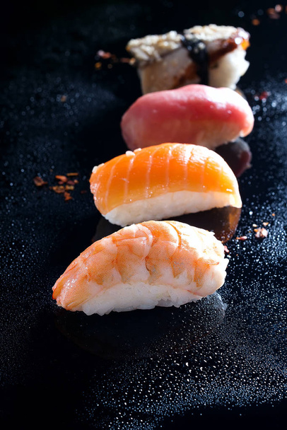 Sashimi, uramaki y nighiri, plato japonés compuesto de arroz, salmón o atún, camarones en negro con gotas de agua. Concepto de restaurante japonés
 - Foto, Imagen