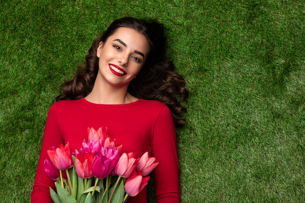 Attractive brunette with tulips on green grass  - Фото, зображення