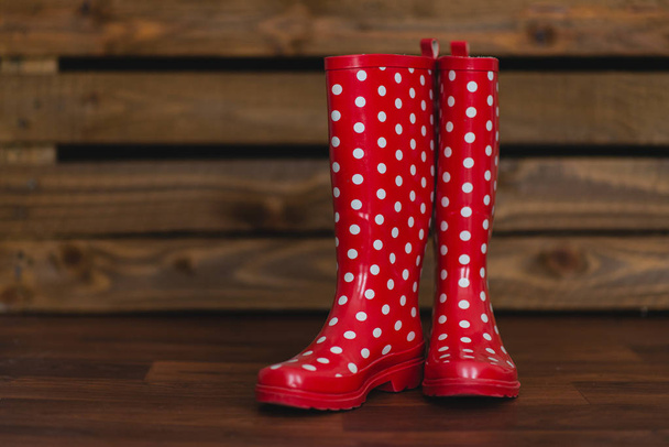 Červené gumové boty s bílými puntíky na dřevěné pozadí - Fotografie, Obrázek