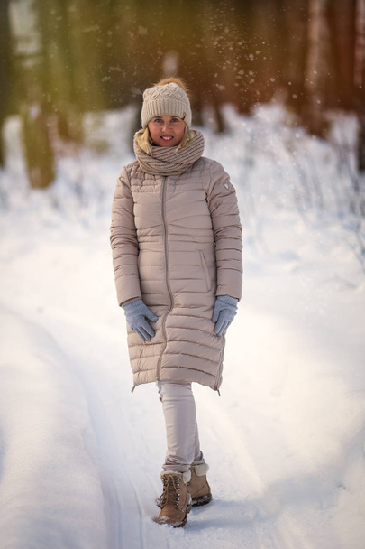 Winter fashion portrait of blonde woman walking in snow park. Cold season - 写真・画像