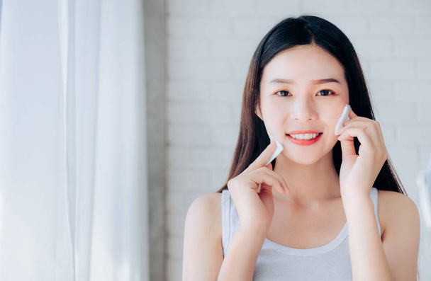 Mladá kráska tvář Asijské žena čištění bavlny jasná tvář kosmetika a ranní úsměv v bílé ložnici, kopírovat prostor. - Fotografie, Obrázek